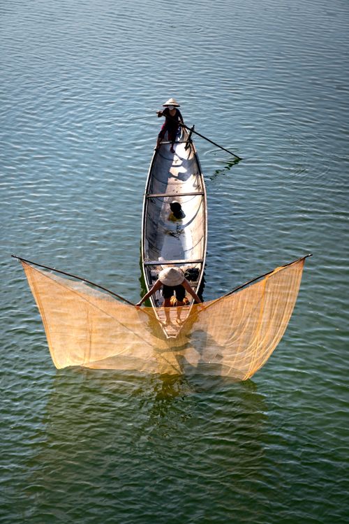 Free Aerial view of fishermen casting nets from a wooden boat in a serene lake setting. Stock Photo