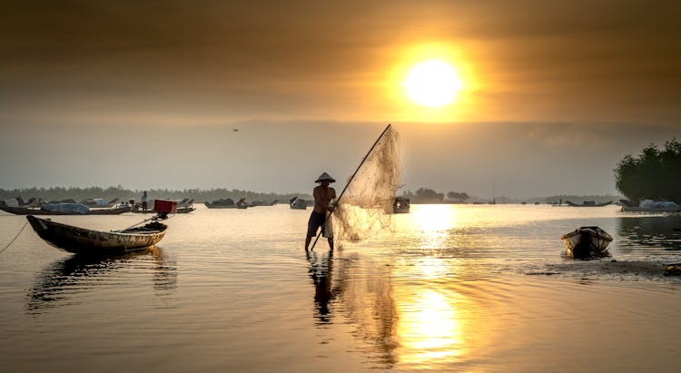 Fisherman With Net In Water At Dawn