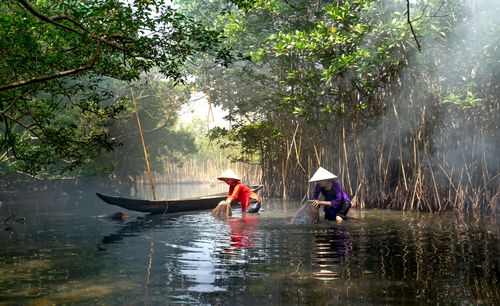 Free Two women using traditional bamboo baskets to fish in a serene river setting. Stock Photo