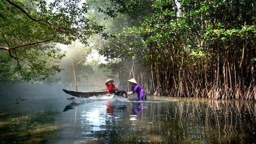 Free Two women navigate a calm river surrounded by lush greenery in rural tranquility. Stock Photo