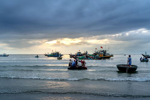 Free Fishermen navigating basket boats in the ocean with a cloudy sky at sunrise. Stock Photo