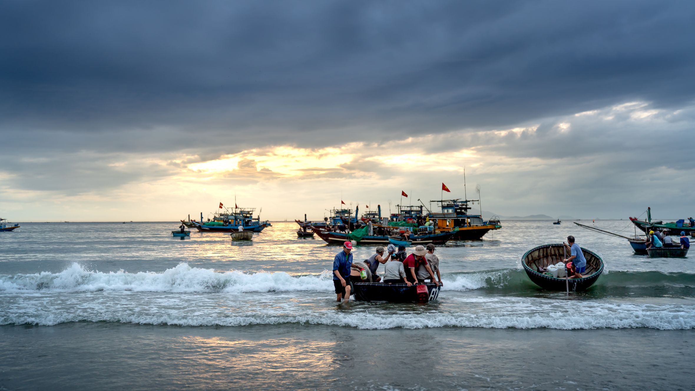 Fishermen work with traditional basket boats on a peaceful beach at sunrise with cloudy skies.
