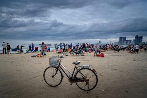 Free A bicycle stands on a beach as people gather near the shore with a distant city skyline. Stock Photo