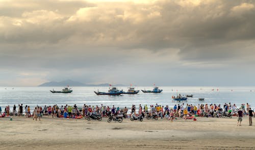 People on Beach Looking at Ships in Sea on Sunset