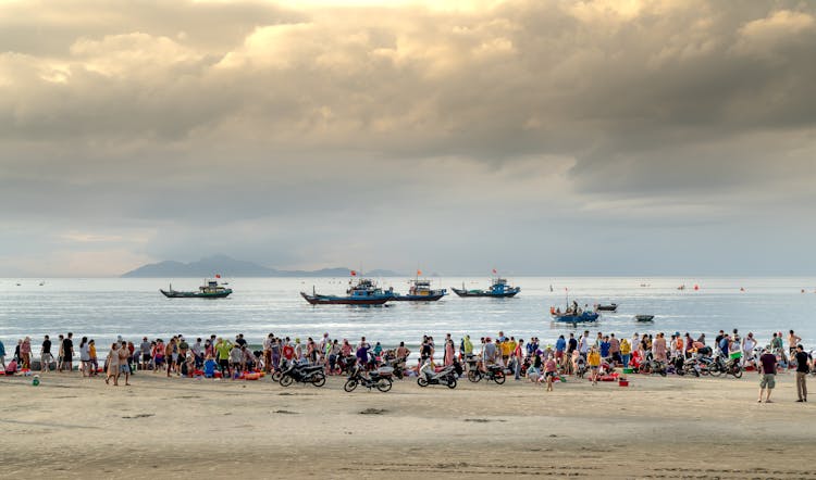 People On Beach Looking At Ships In Sea On Sunset