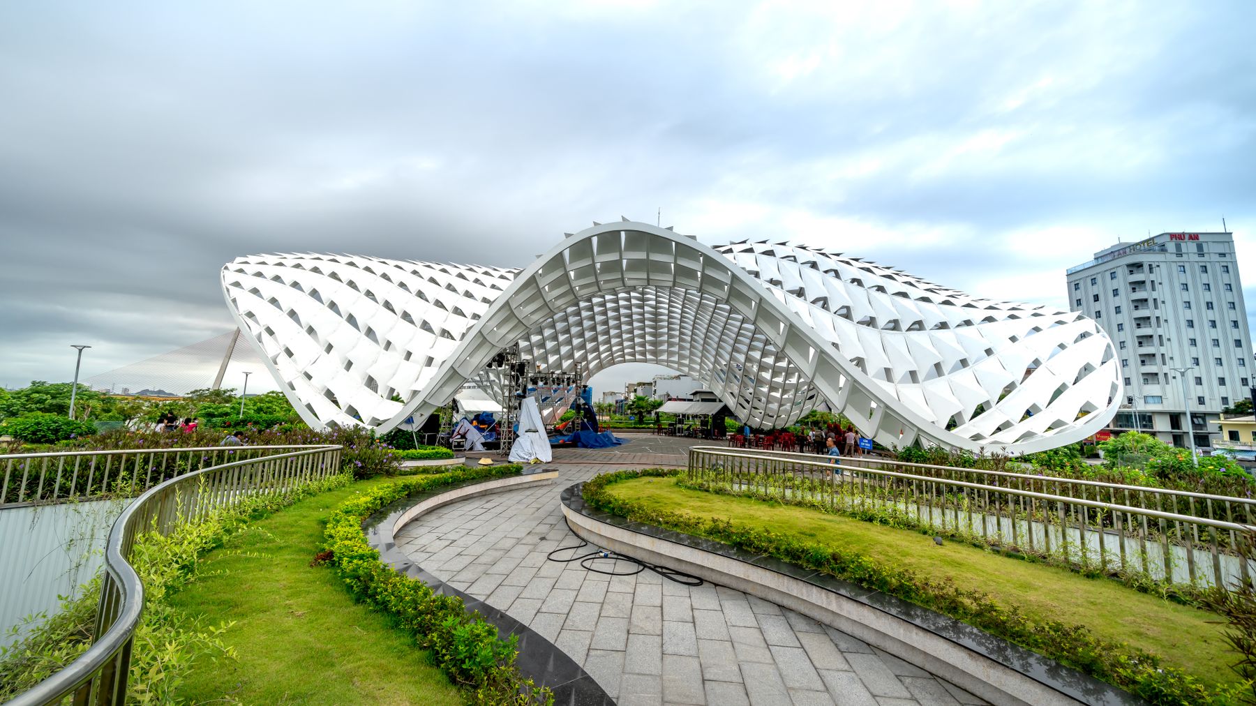 Striking modern architectural structure in Vietnam park with green walkways and urban backdrop.