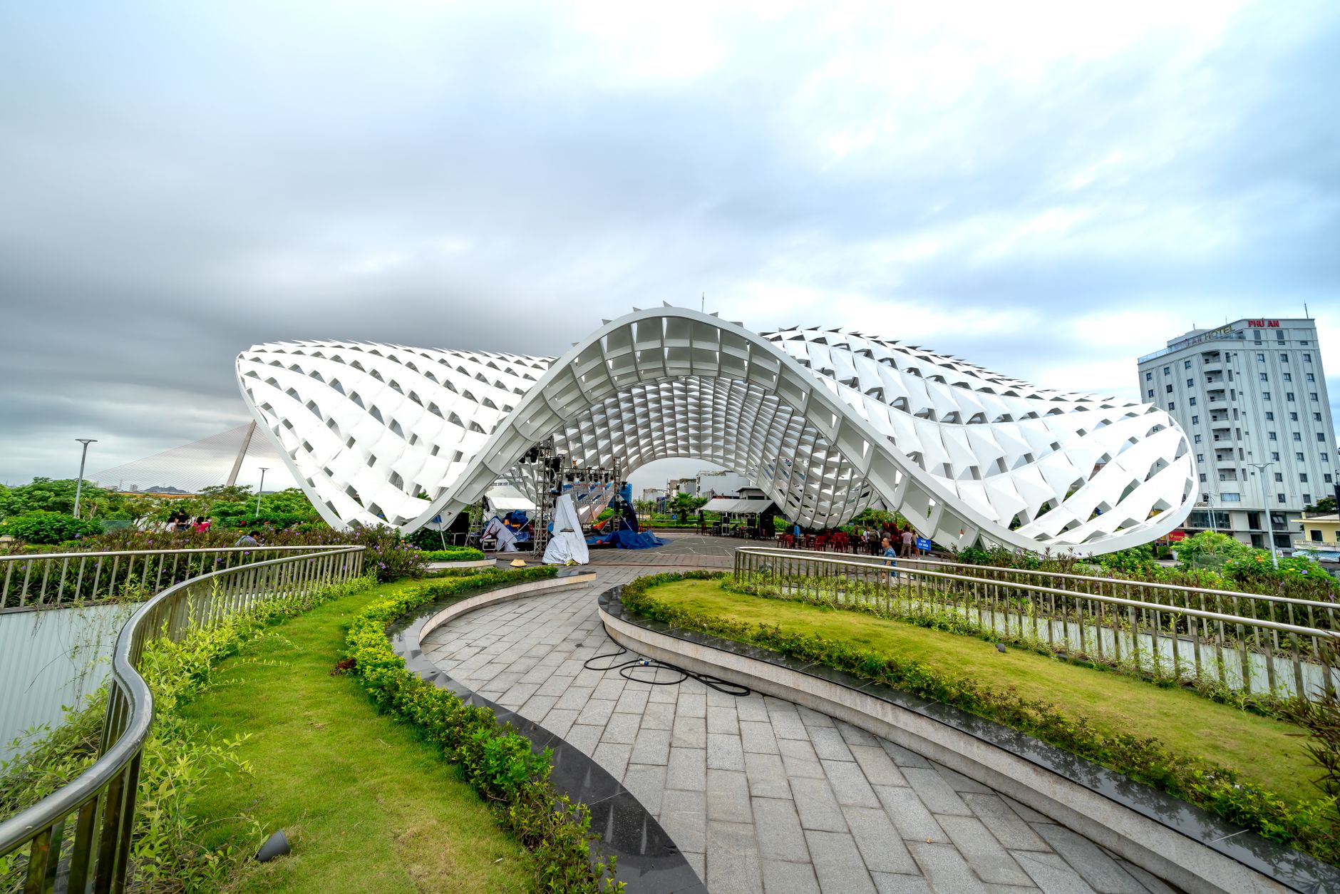 Striking modern architectural structure in Vietnam park with green walkways and urban backdrop.