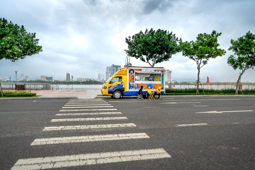 A vibrant food truck parked on an empty city street with a scenic riverside view.
