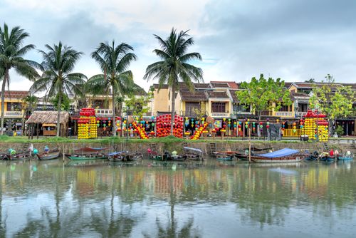 Free Vibrant riverfront with colorful lanterns and boats in a picturesque cityscape. Stock Photo