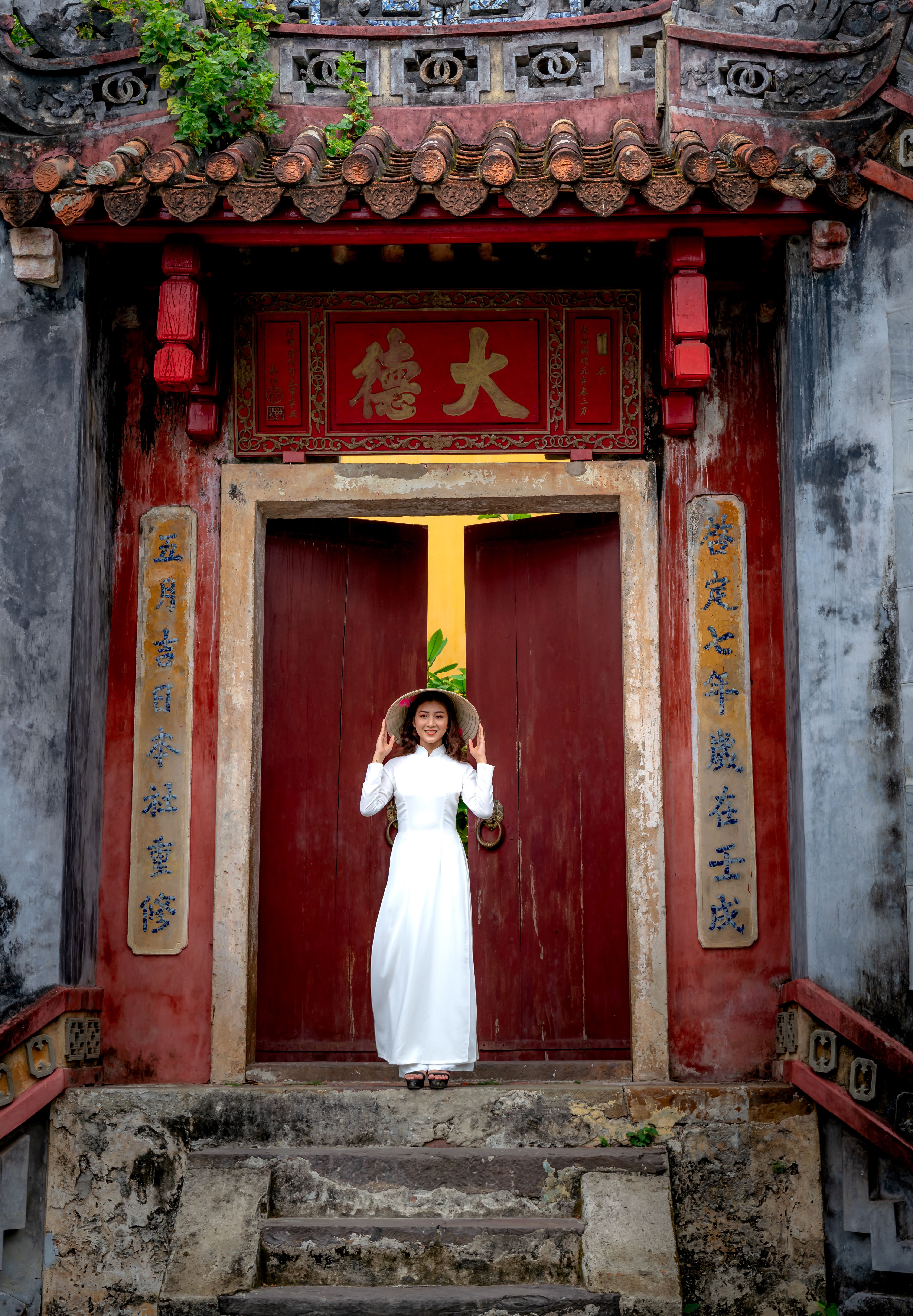 Woman in traditional ao dai dress stands gracefully at historic Ba Mu Temple gate in Hoi An, Vietnam.