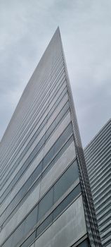 Low angle view of a modern skyscraper with a sleek, reflective facade against a cloudy sky.