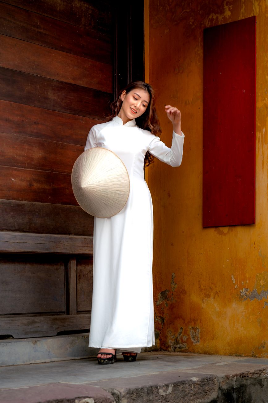 A woman in traditional ao dai standing gracefully, holding a Vietnamese conical hat.