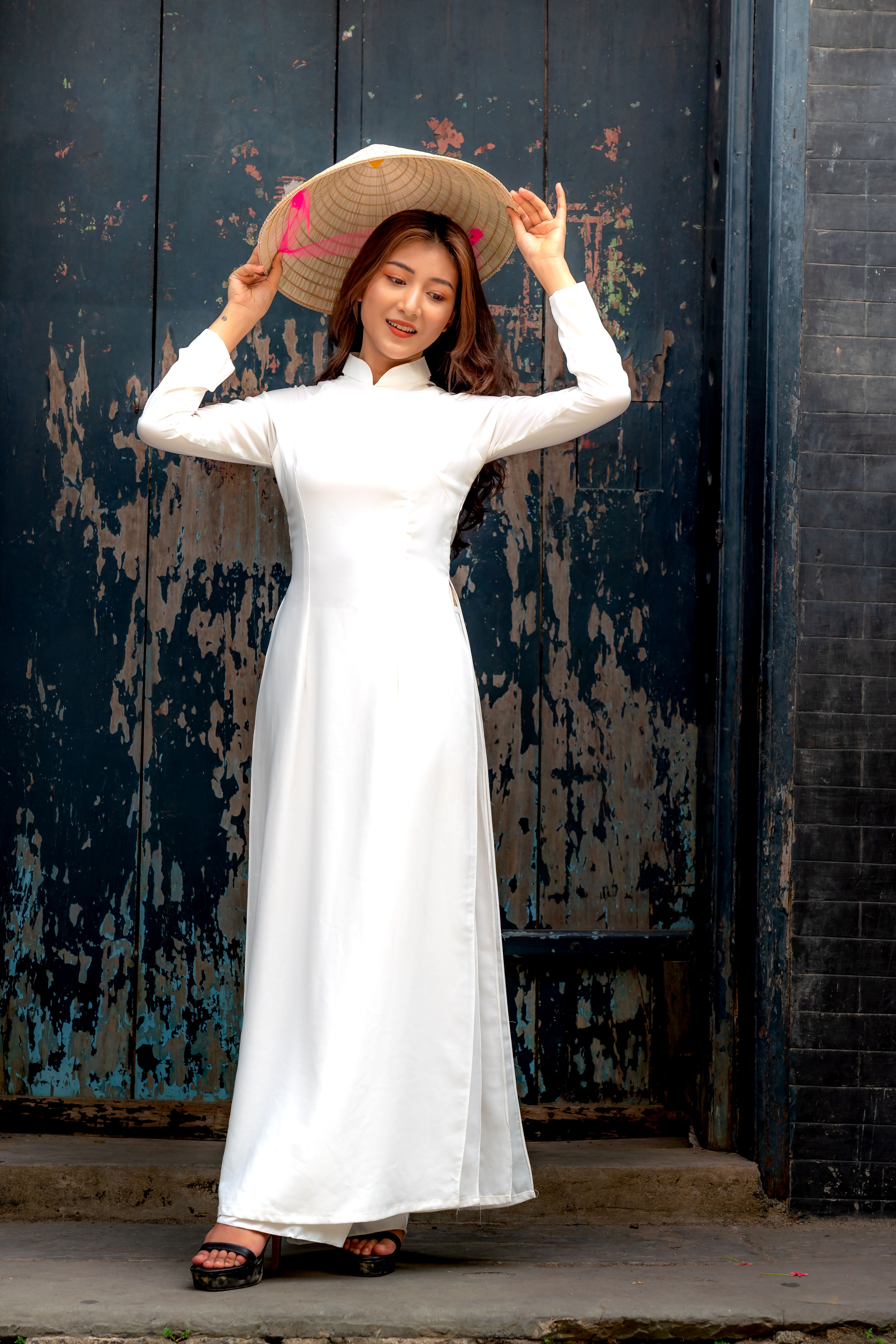 Portrait of a young woman wearing a traditional white dress and conical hat standing outside.