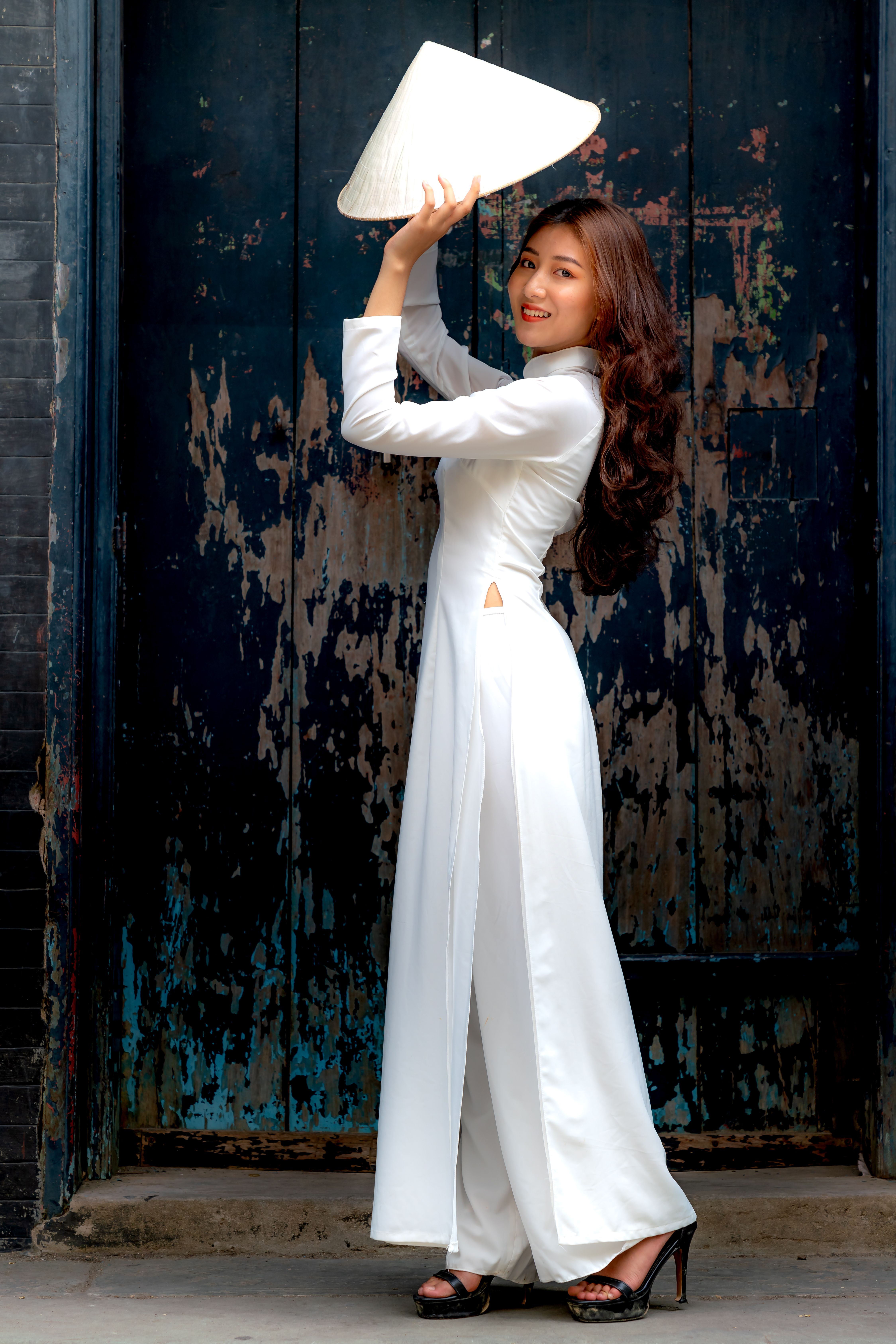 Elegant woman wearing ao dai and holding a conical hat, posing outdoors.