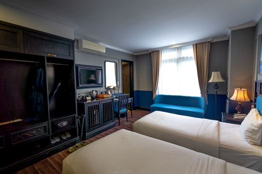 Spacious hotel room with twin beds, modern amenities, and elegant decor illuminated by natural light.