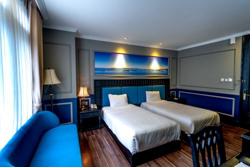 Free Stylish hotel room featuring blue decor, twin beds, and modern furnishings with ample natural light. Stock Photo