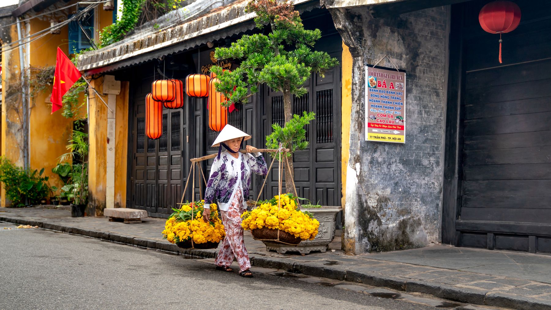 Một phụ nữ Việt Nam mang hoa trên con phố truyền thống ở Hội An, Việt Nam.