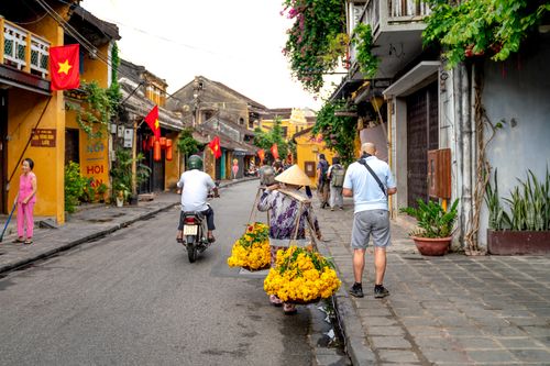 Free Vibrant street scene in Hoi An with vendor and motorbike amidst historic buildings. Stock Photo