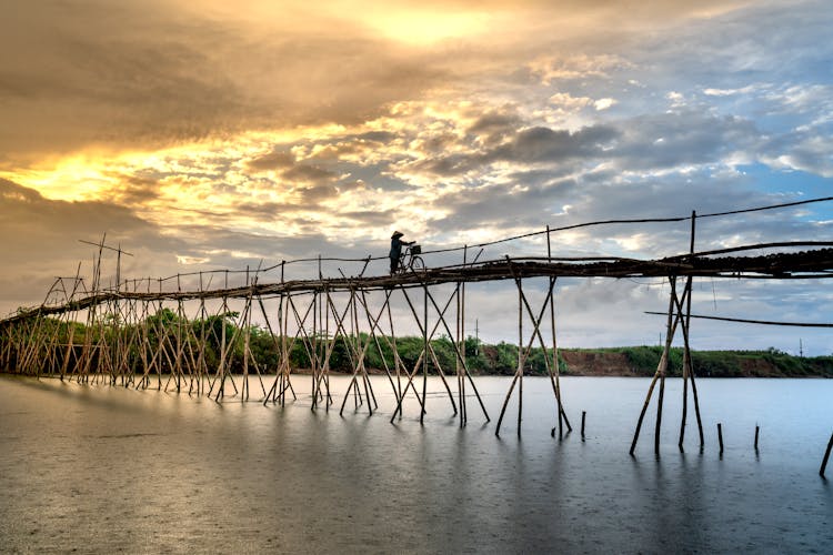 A Person With A Bicycle Crossing A Wooden Footbridge