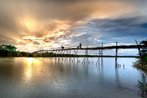 Free Silhouettes of people walking on a rustic wooden bridge over a river at sunset, creating a serene and picturesque scene. Stock Photo