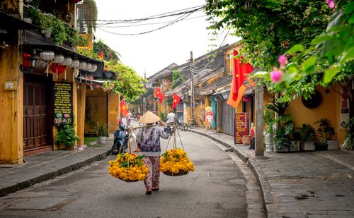 Free A vendor in a conical hat walks with flowers on a vibrant Vietnamese street. Stock Photo