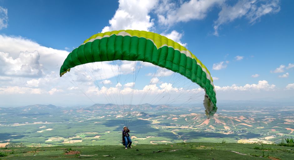 A paraglider takes off from a hilltop, enjoying a sunny day with panoramic views of the landscape below.