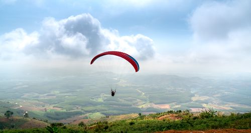 Free Paraglider soaring over a lush valley under a blue sky, embracing the thrill of adventure. Stock Photo