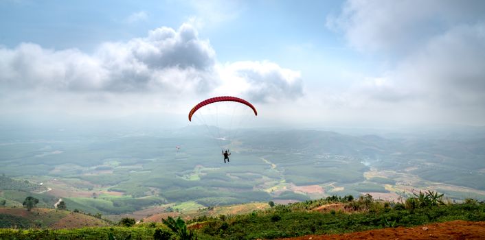 A paraglider soars through a cloudy sky offering a breathtaking aerial view of the valley below.