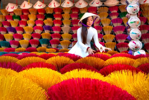 Free Woman in traditional Ao Dai arranging colorful incense sticks outdoors in Vietnam. Stock Photo