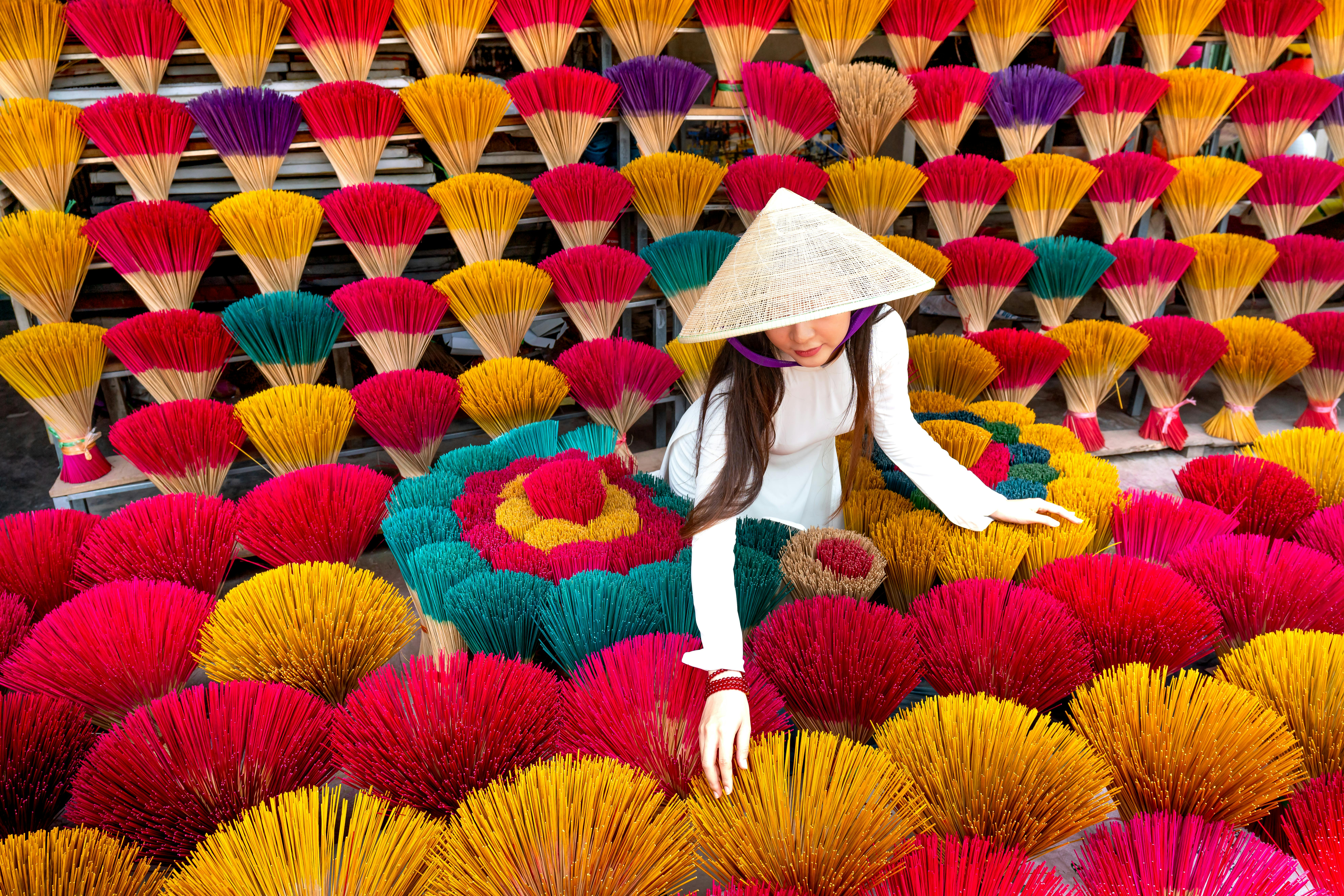 A woman in traditional attire arranges vibrant incense sticks, showcasing cultural craft.