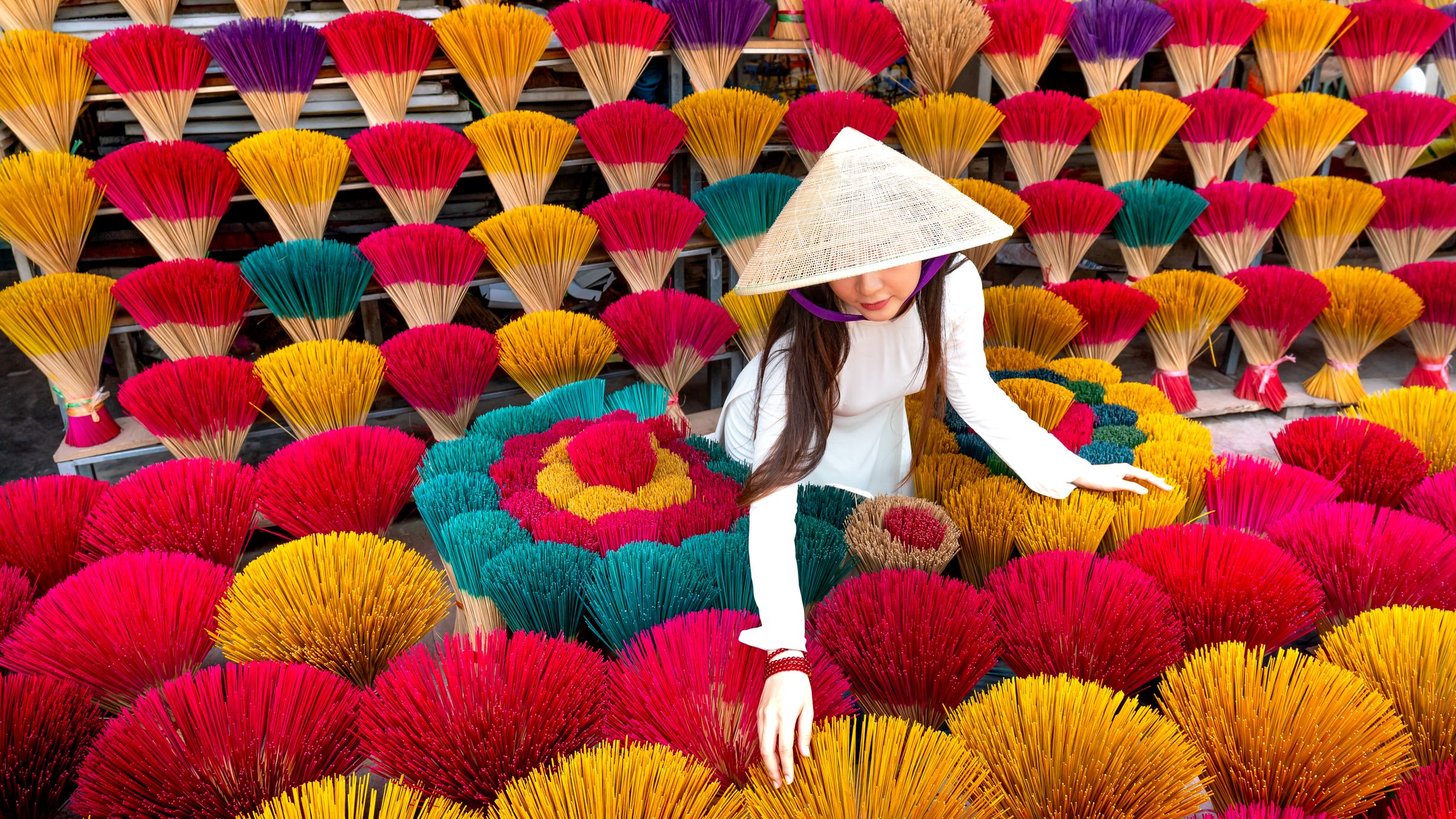A woman in traditional attire arranges vibrant incense sticks, showcasing cultural craft.