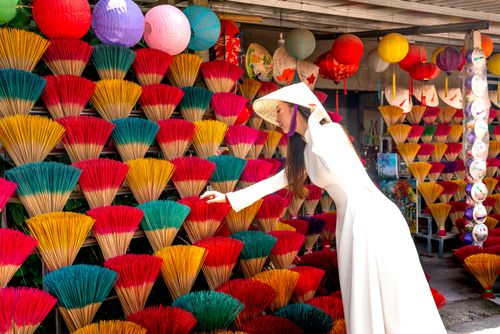 Free A woman in a traditional ao dai selects colorful incense sticks at an outdoor market Stock Photo