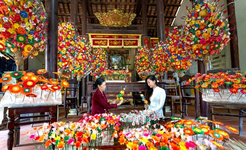Free Women crafting vibrant paper flowers in a Vietnamese temple setting. Stock Photo