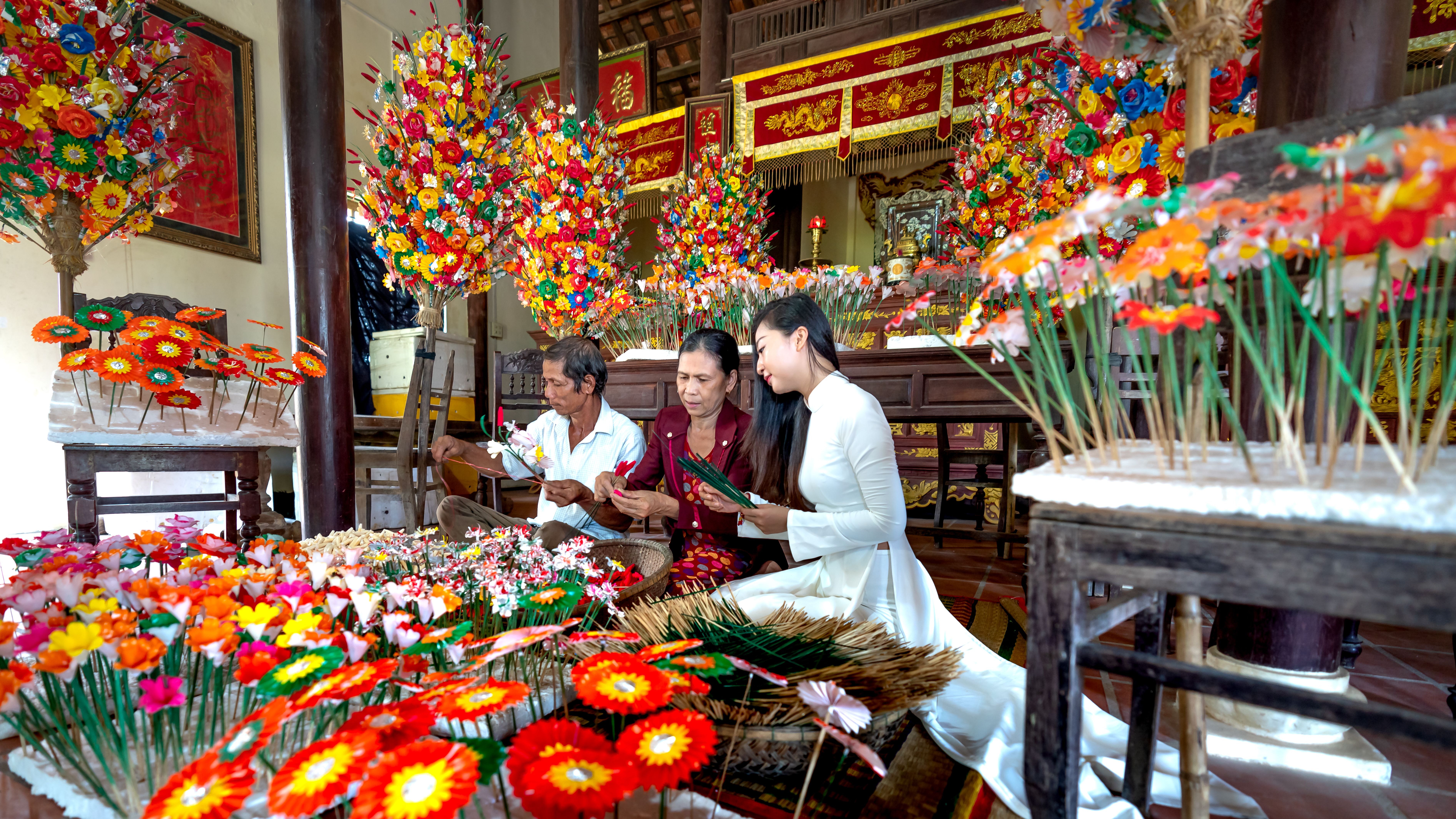 Asian artisans crafting vibrant paper flowers in a traditional setting, showcasing cultural heritage.