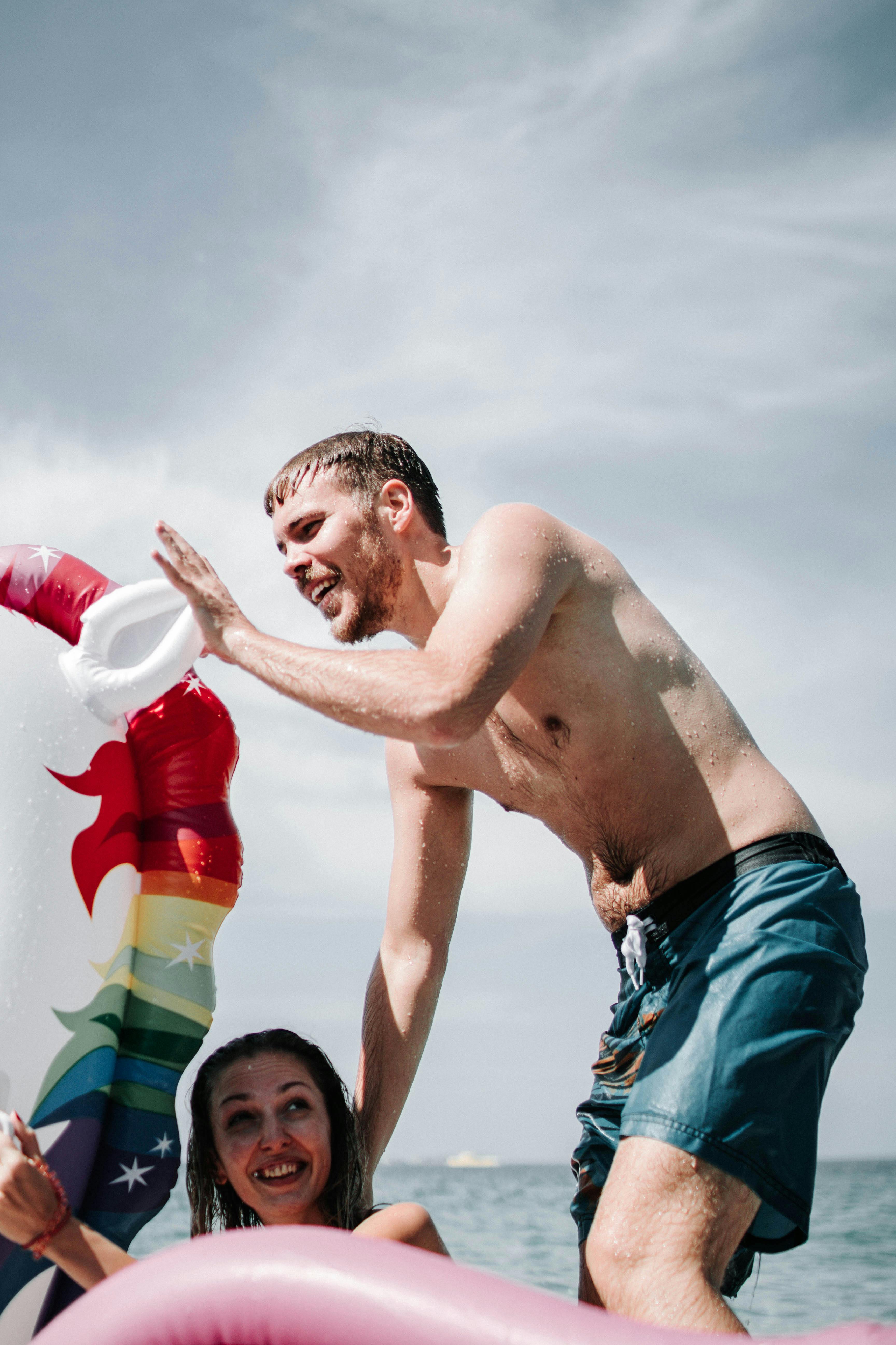 微笑的年轻人在阳光明媚的海滩享受了一天，还在海中玩着五颜六色的充气玩具