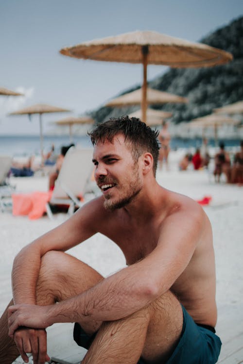 Free Man Sitting on Sand with Hands Crossed over his Knees Stock Photo