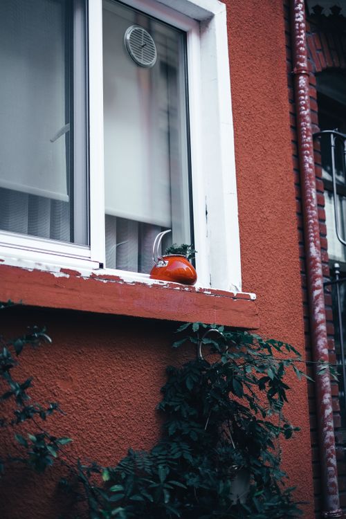 Free A red building facade featuring a window with a kettle on the sill, adding an artistic touch. Stock Photo
