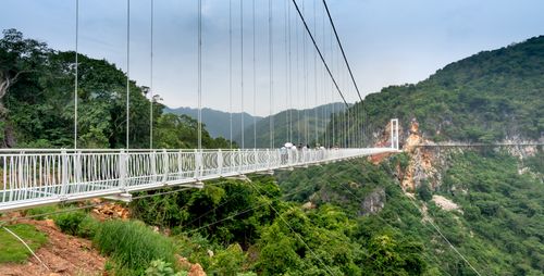 Free A stunning suspension bridge stretches over a verdant valley with distant mountains. Stock Photo
