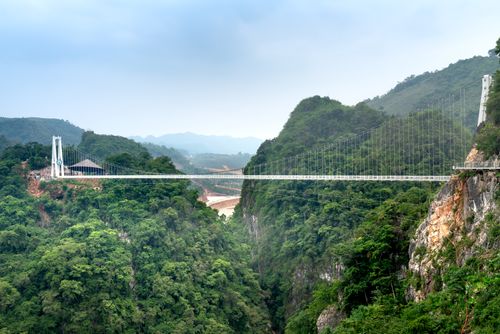 Free Stunning modern suspension bridge spans a lush green valley with mountainous backdrop. Stock Photo