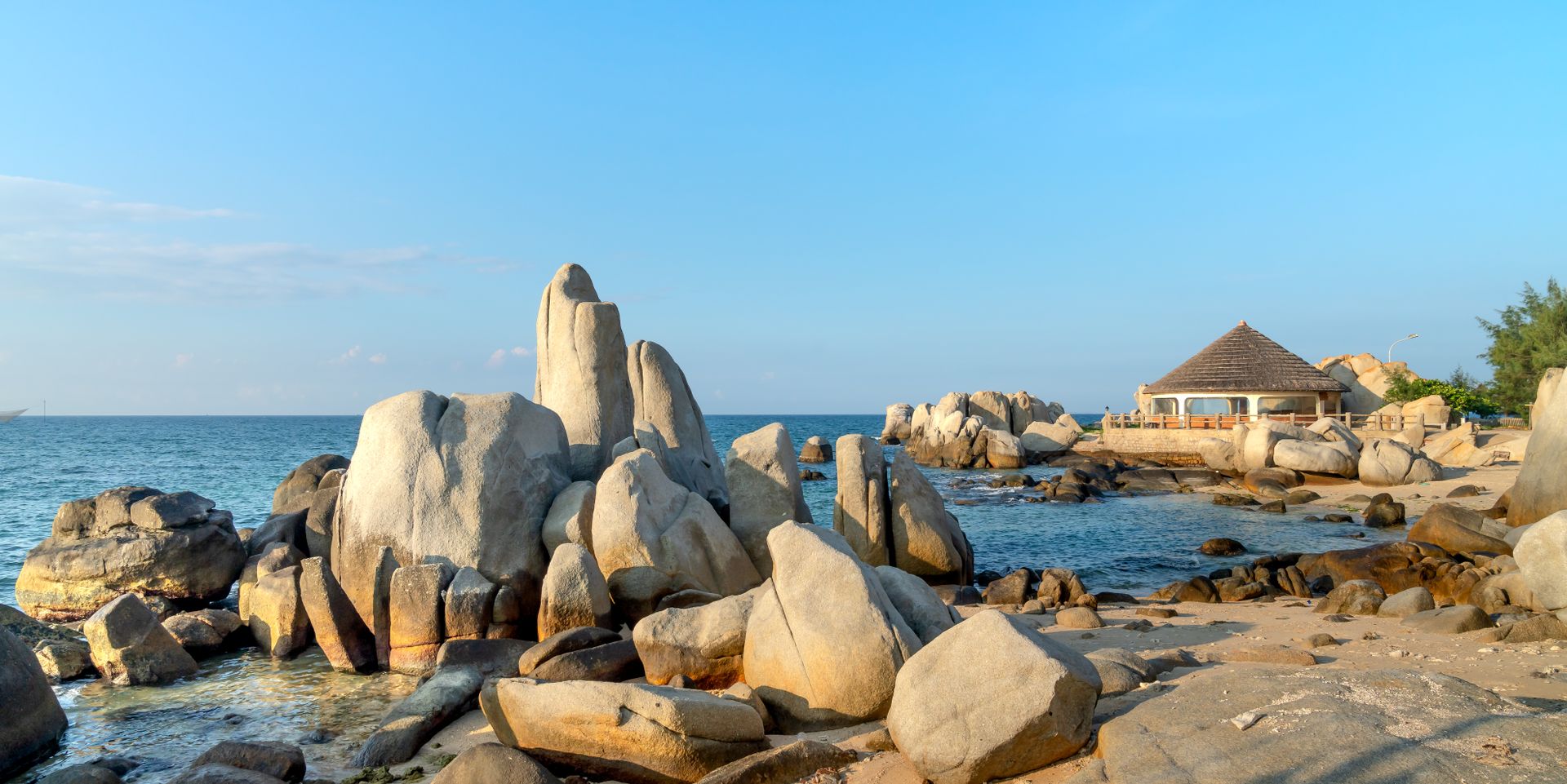 Beautiful beach scene with rock formations and a gazebo by the sea.