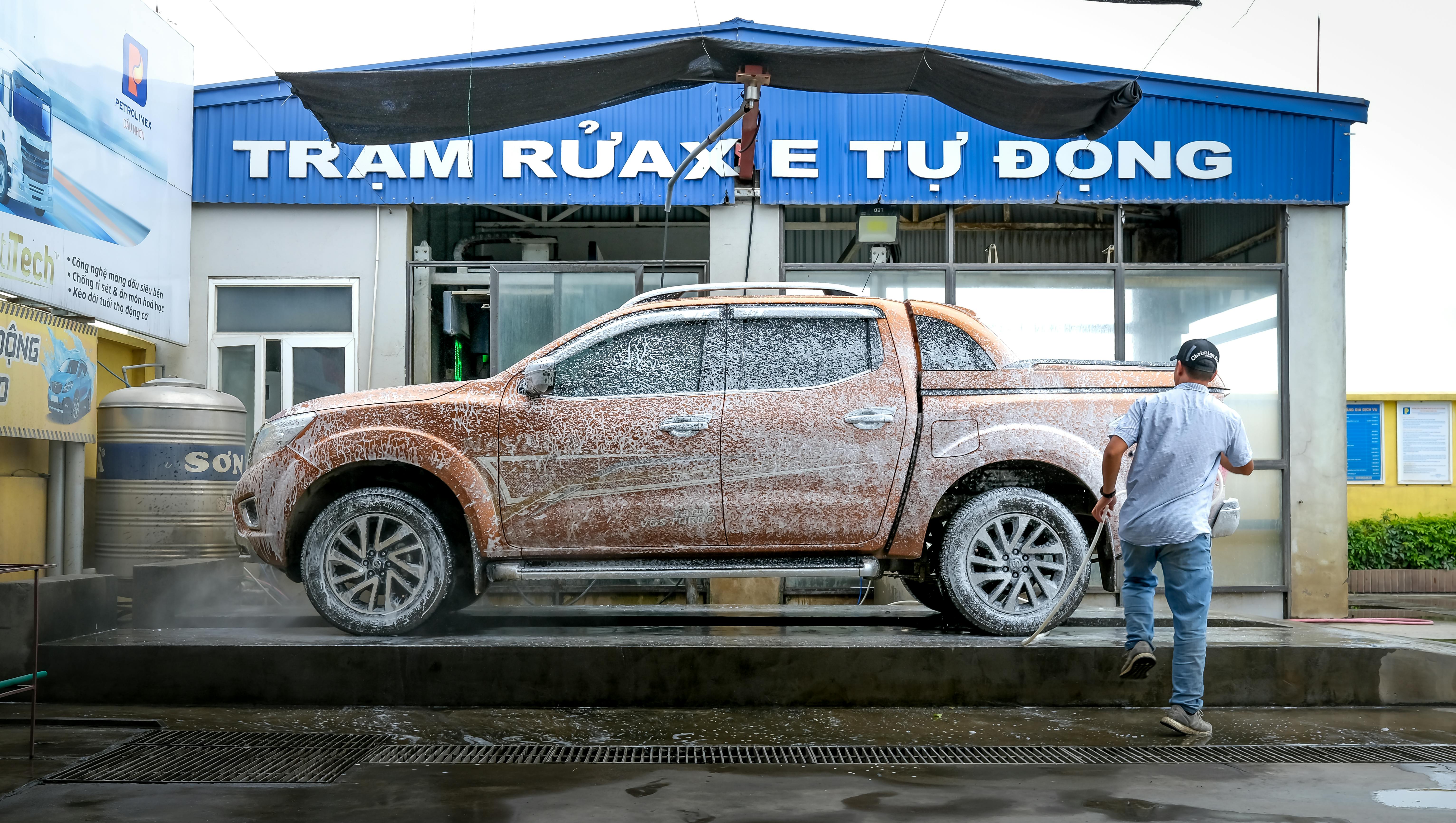 A man cleans a foamy pickup truck at an automatic car wash station outdoors.