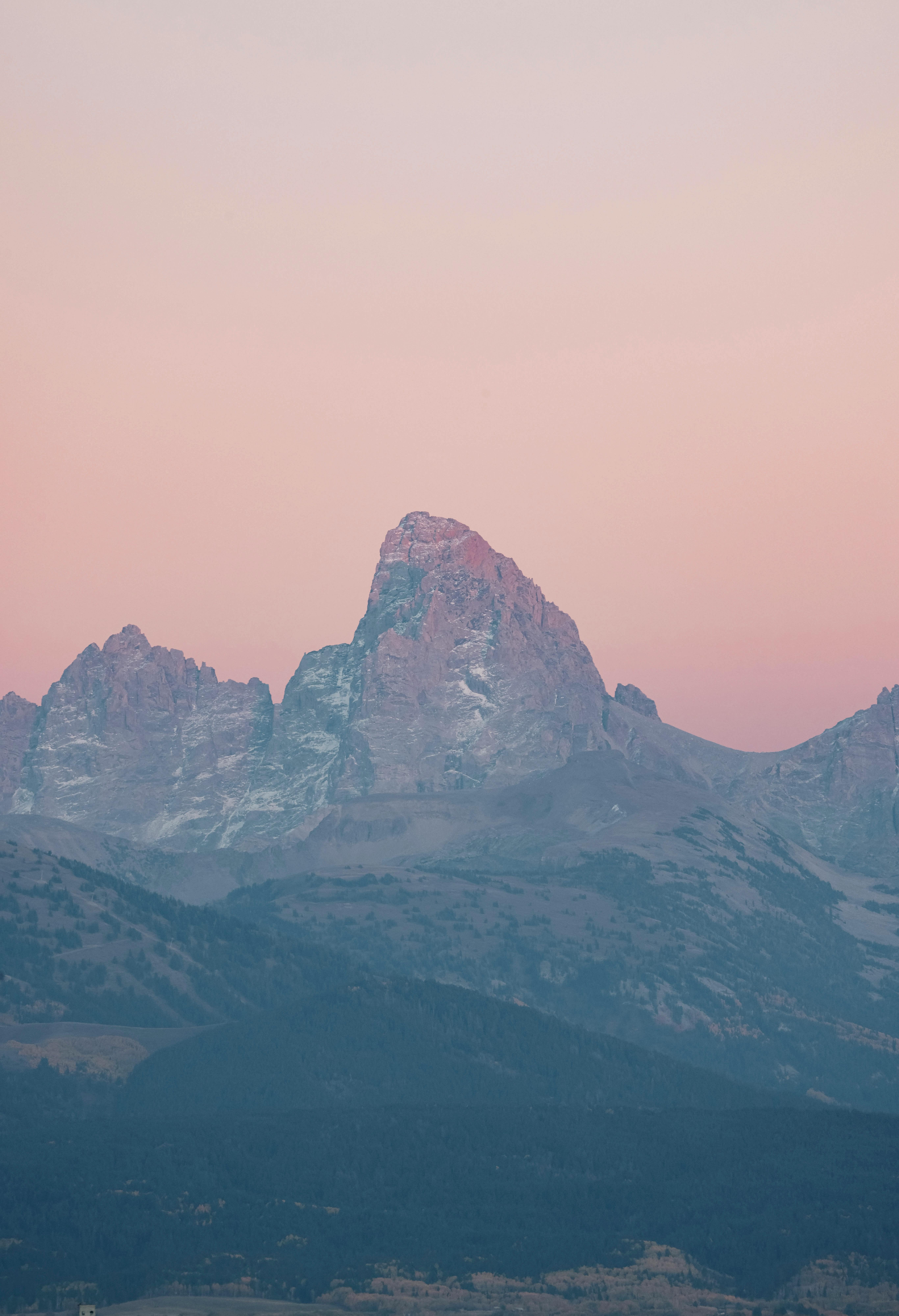 Peaceful twilight view of rugged rocky mountains under a pink-orange sky. Ideal for nature and travel visuals.
