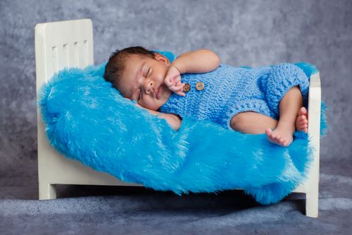 Free A cute baby sleeping peacefully on a miniature bed with a blue crocheted outfit and fluffy blanket. Stock Photo