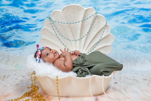 A cute baby in a seashell surrounded by beach-themed decor, showcasing innocence and style.