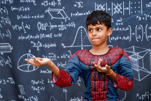 A young boy dressed as a superhero stands confidently in front of a chalkboard filled with math equations.