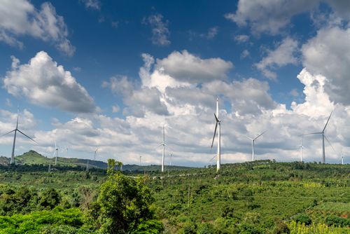 Free A row of wind turbines on a green hillside under a bright blue sky with clouds. Stock Photo