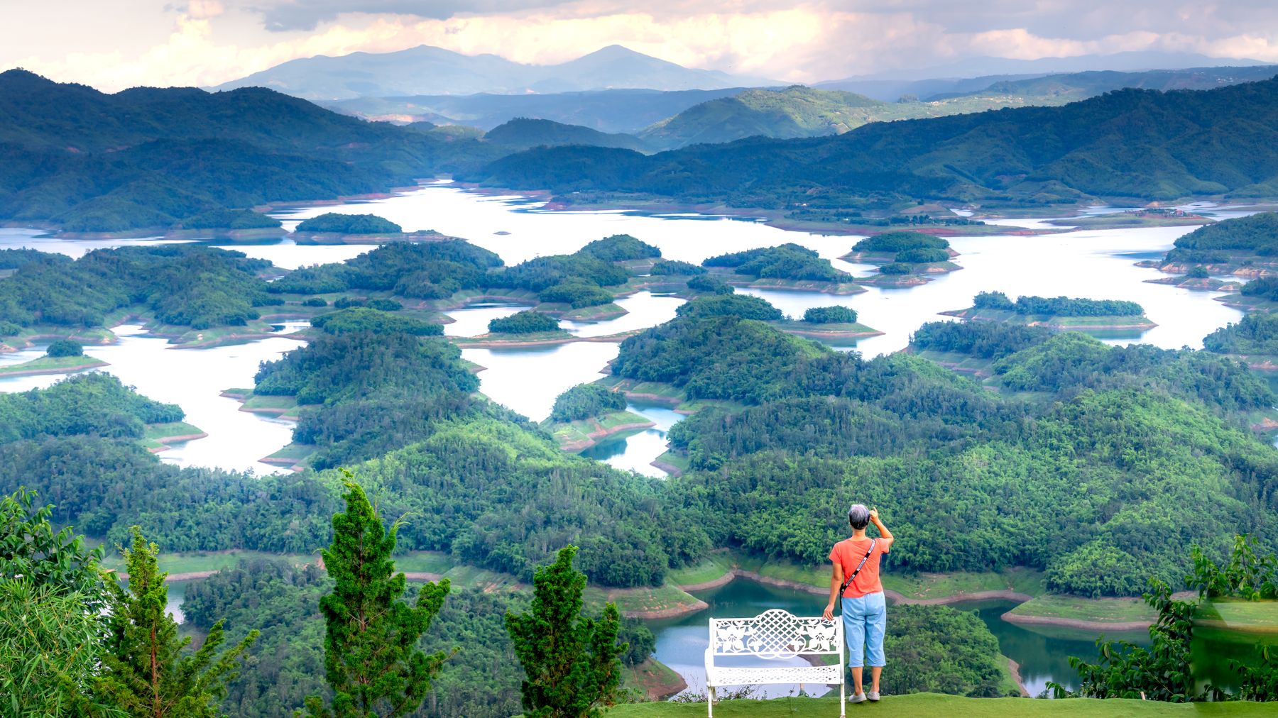 Woman admires picturesque landscape of lush hills and lakes from a viewpoint in Vietnam.
