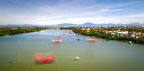 Free Aerial shot of vibrant fishing nets in a tranquil river with town and mountain backdrop. Stock Photo