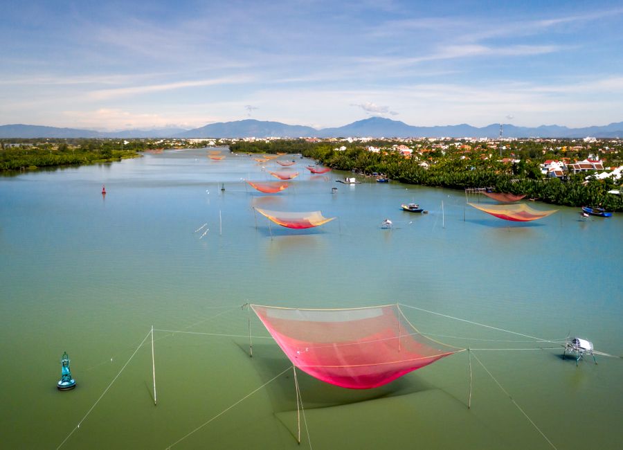 Beautiful aerial view of colorful fishing nets on a serene river surrounded by lush greenery and distant mountains.
