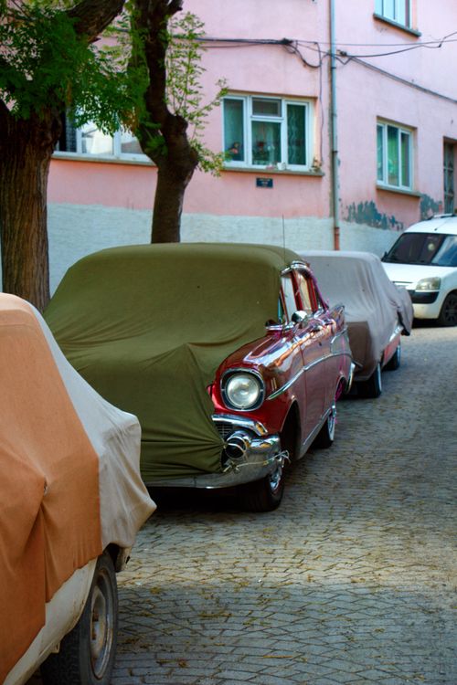 Free A row of vintage cars covered with fabric parked on a cobblestone street in a residential area. Stock Photo